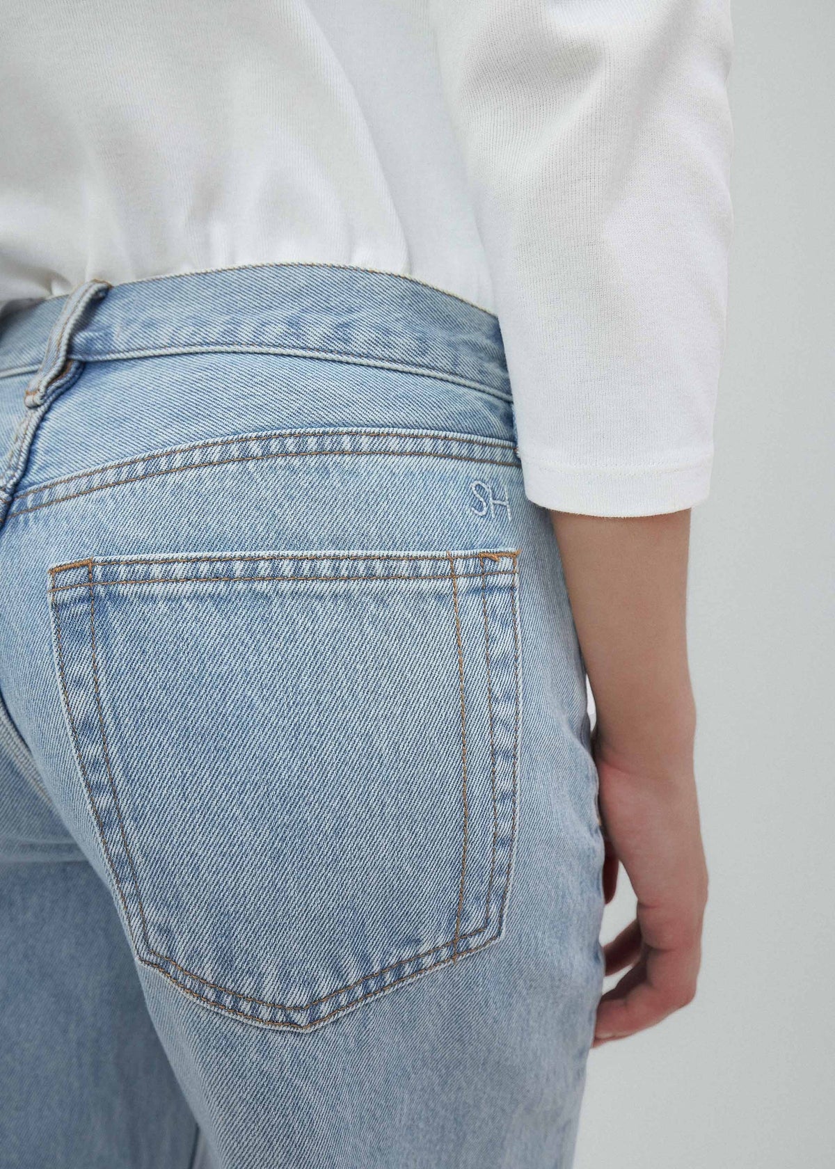 A person is wearing light blue Everyday Jeans and a white long-sleeve shirt, shown from the back and waist down, with one hand resting by their side. The versatile Everyday Jeans feature visible stitching, a relaxed silhouette, and classic back pockets.