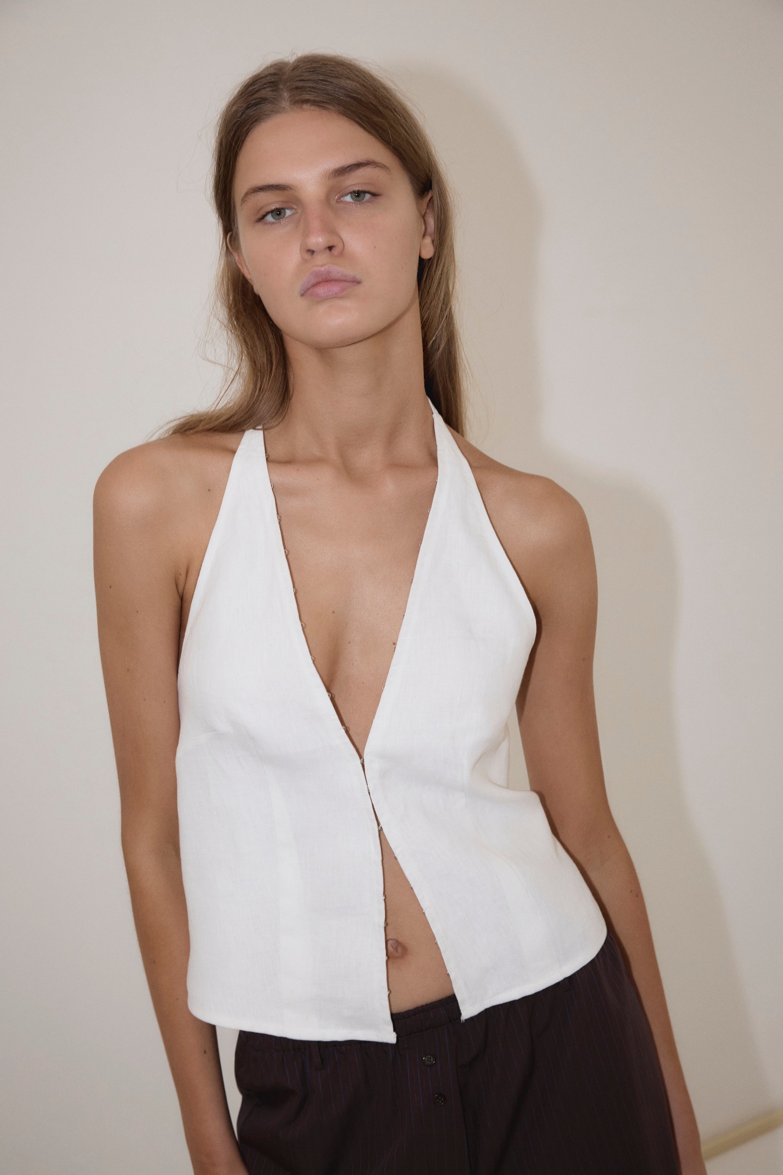A person wearing the Close Halter Top from Deiji Studios paired with dark pants stands against a plain light-colored wall, looking directly at the camera with a neutral expression.