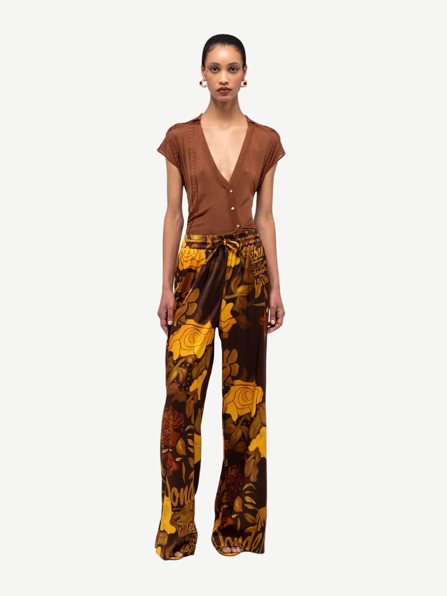 Woman wearing a brown top and patterned pants on a white background