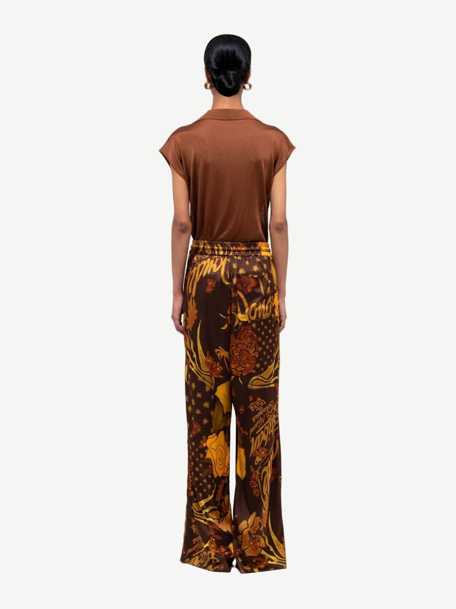 Person wearing a brown top and patterned pants on a white background
