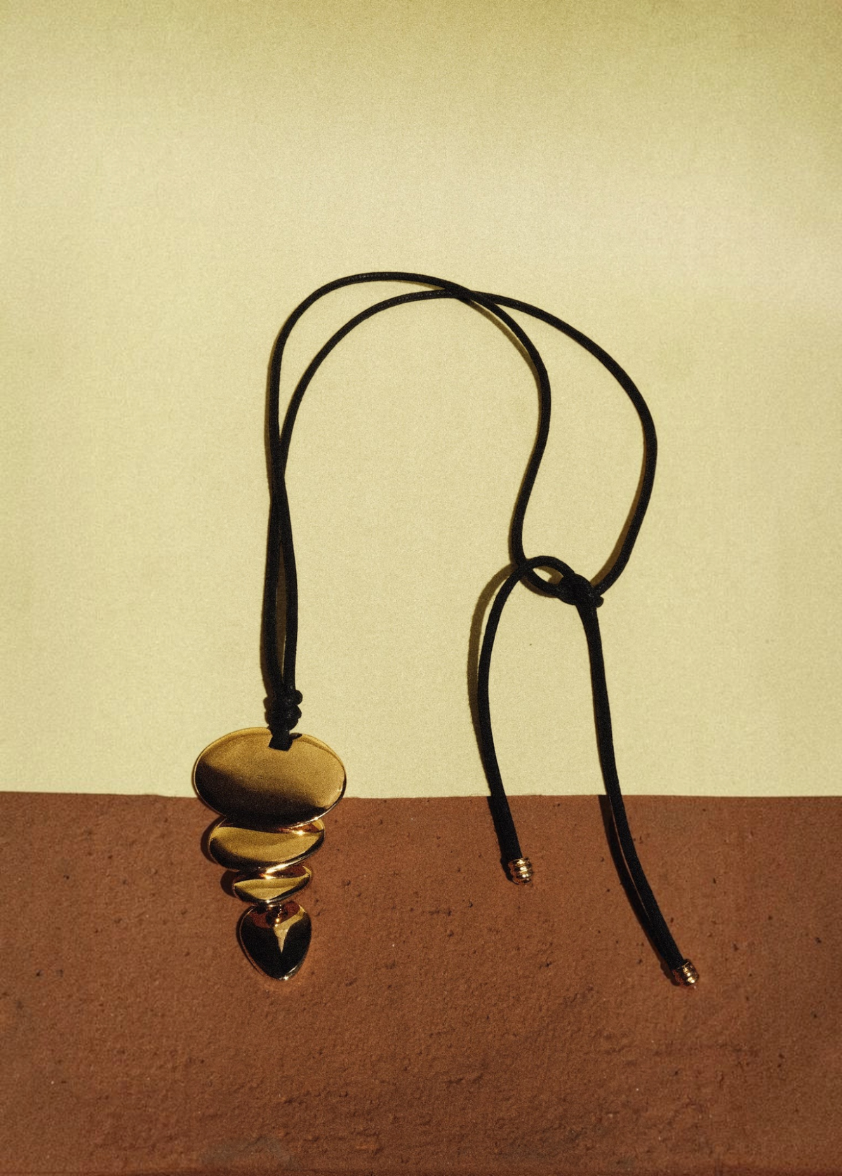 KABE SHOP INC gold pendant necklace featuring a sculptural layered design on a long black cord