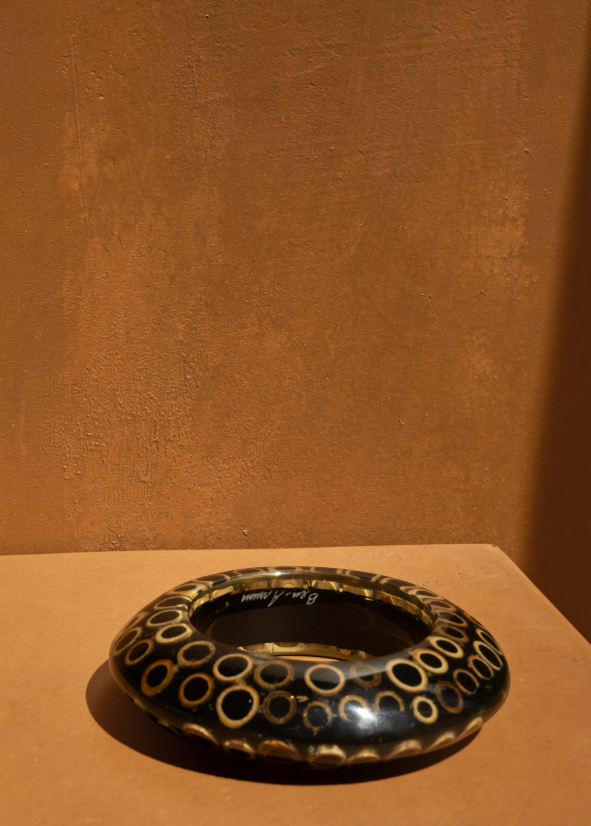 KABE SHOP INC wood and resin bangle featuring a black and tan circular pattern in a sculptural, modern design.