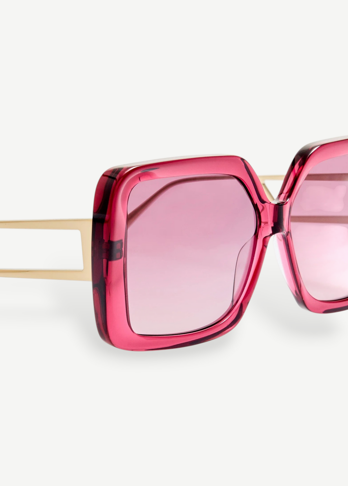 Close-up of the Macy Sunglasses, showcasing oversized square frames crafted from bold pink Italian acetate, with pink tinted lenses and gold plated temples set against a plain white background.