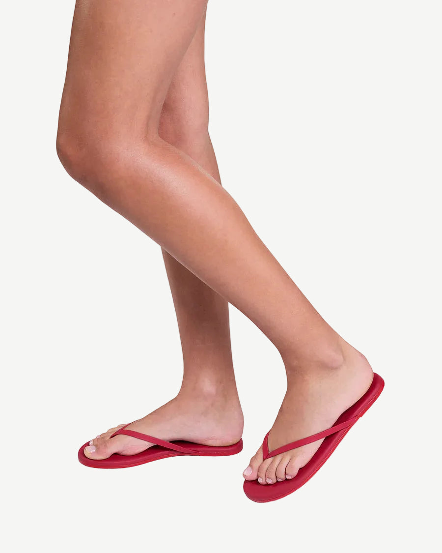 Red flip-flops worn on feet against a white background