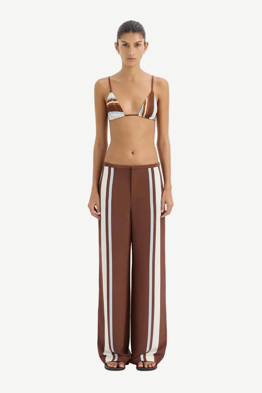 Woman wearing a brown and white striped bikini with matching pants on a white background