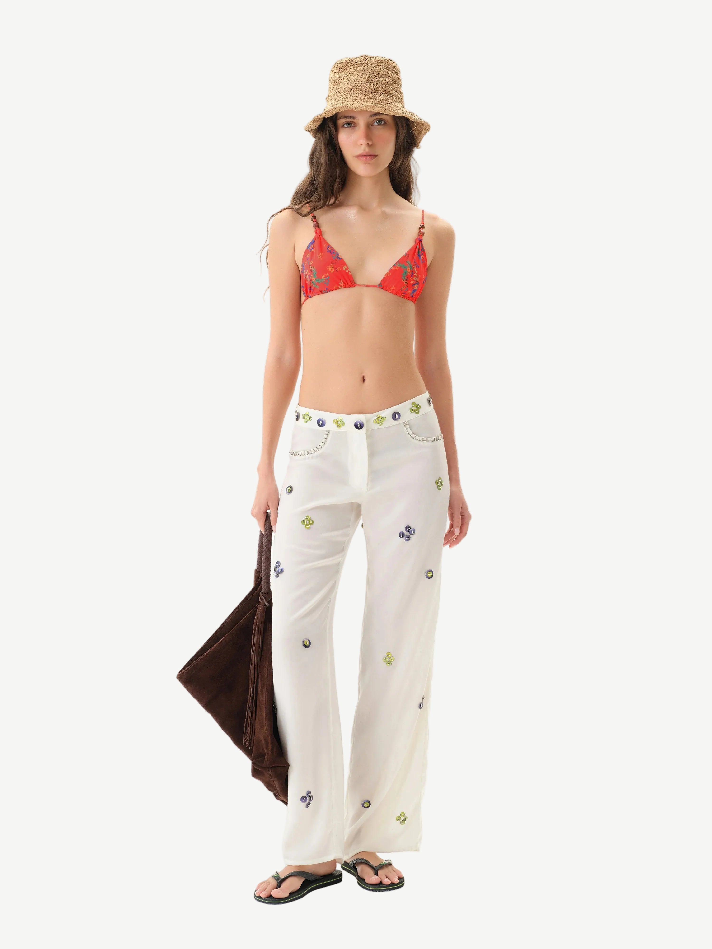 Woman wearing a red bikini top and white pants with colorful patterns on a white background