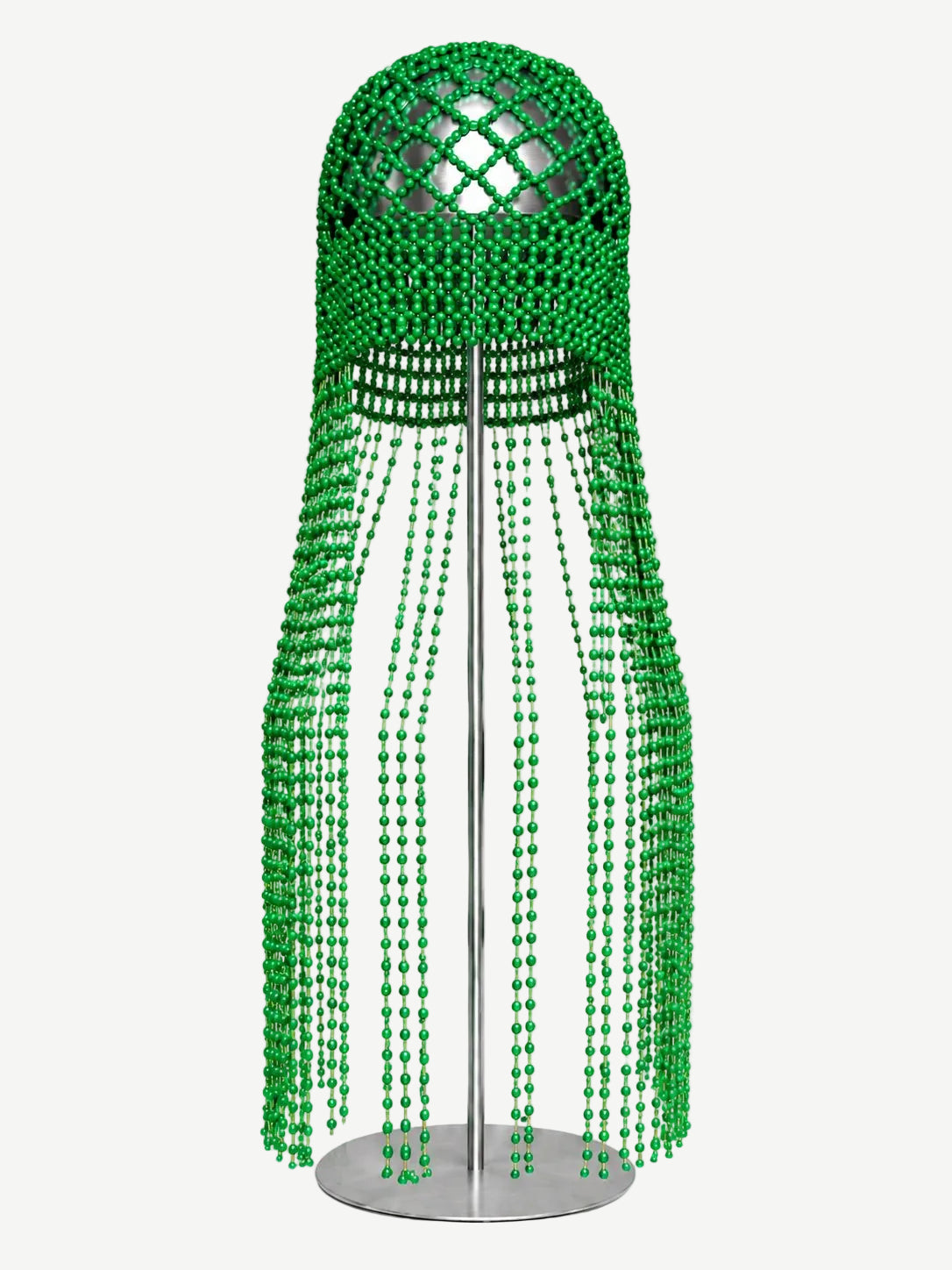 The Beaded Headpiece features handcrafted green bead strands arranged in a dome shape on a stand. Long, curtain-like rows of beads drape downward to create a sculptural cap effect, beautifully displayed against a white background.