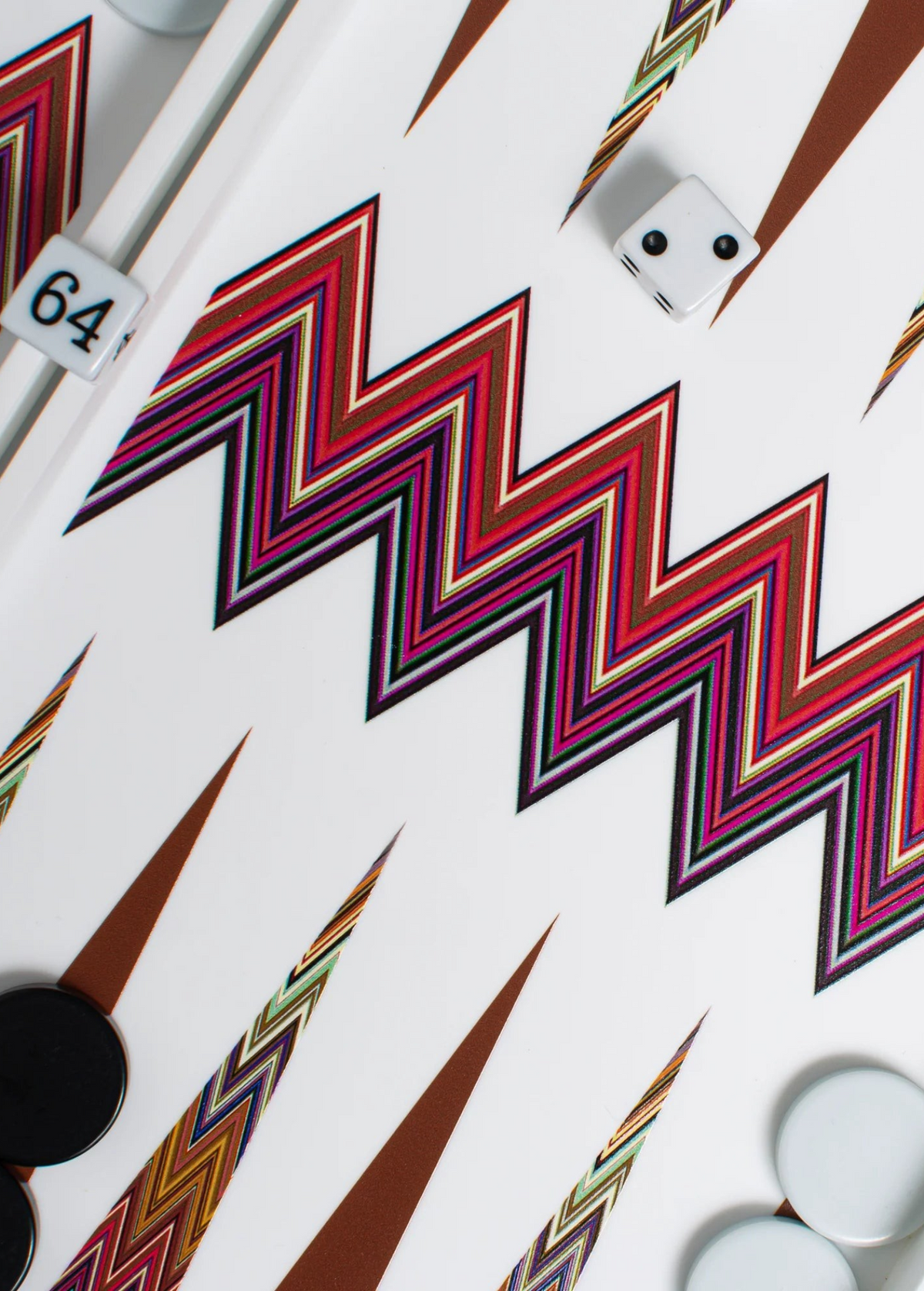 A close-up of the ZigZag Backgammon Board Game, featuring a vibrant acrylic zigzag design with black and white checkers, a doubling cube set to 64, and a white die displaying two dots. The bold zigzag patterns make this board an eye-catching addition to any coffee table.