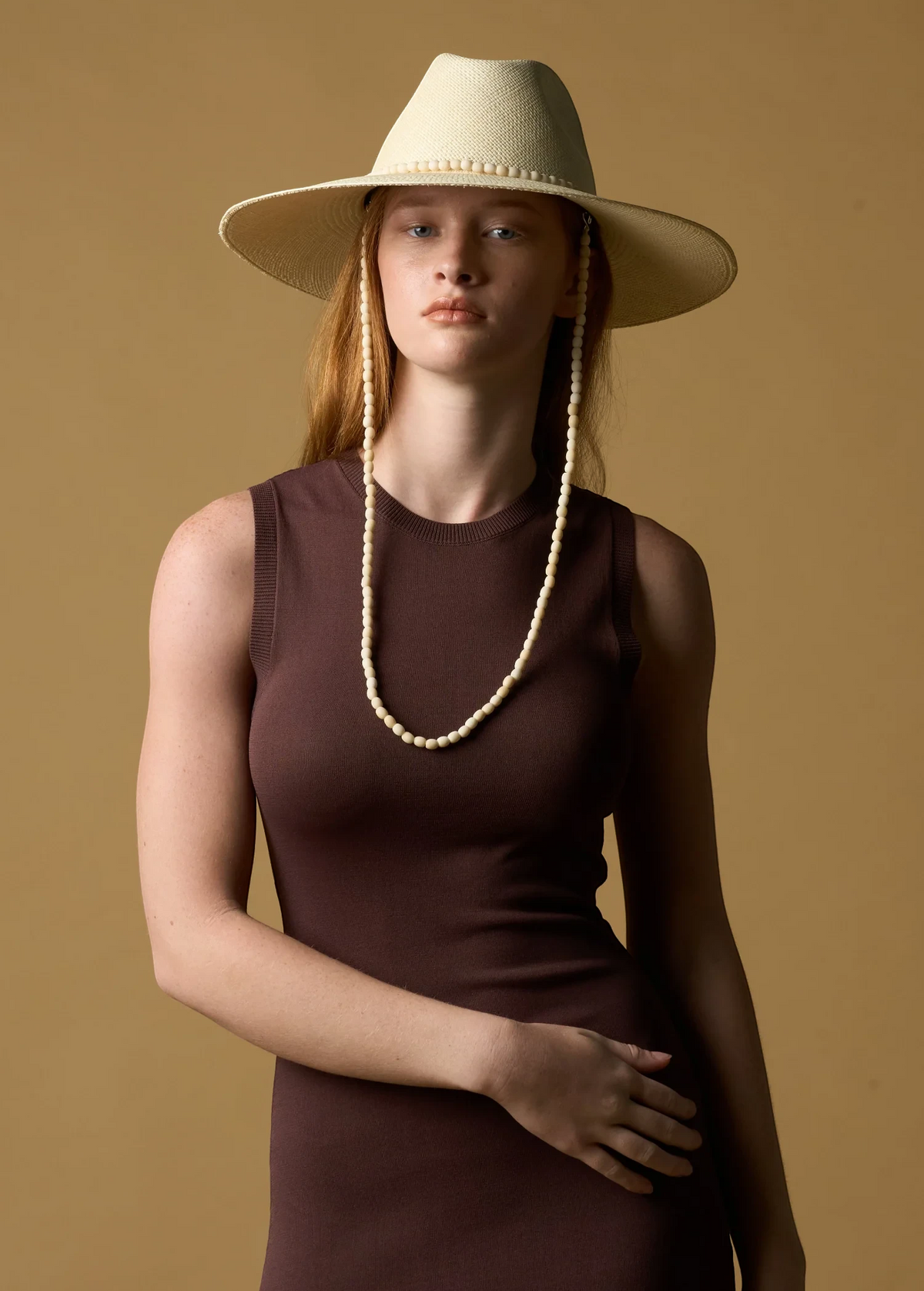Model wearing a KABE SHOP INC Cajas wide brim straw hat with beaded chin strap against a tan background.