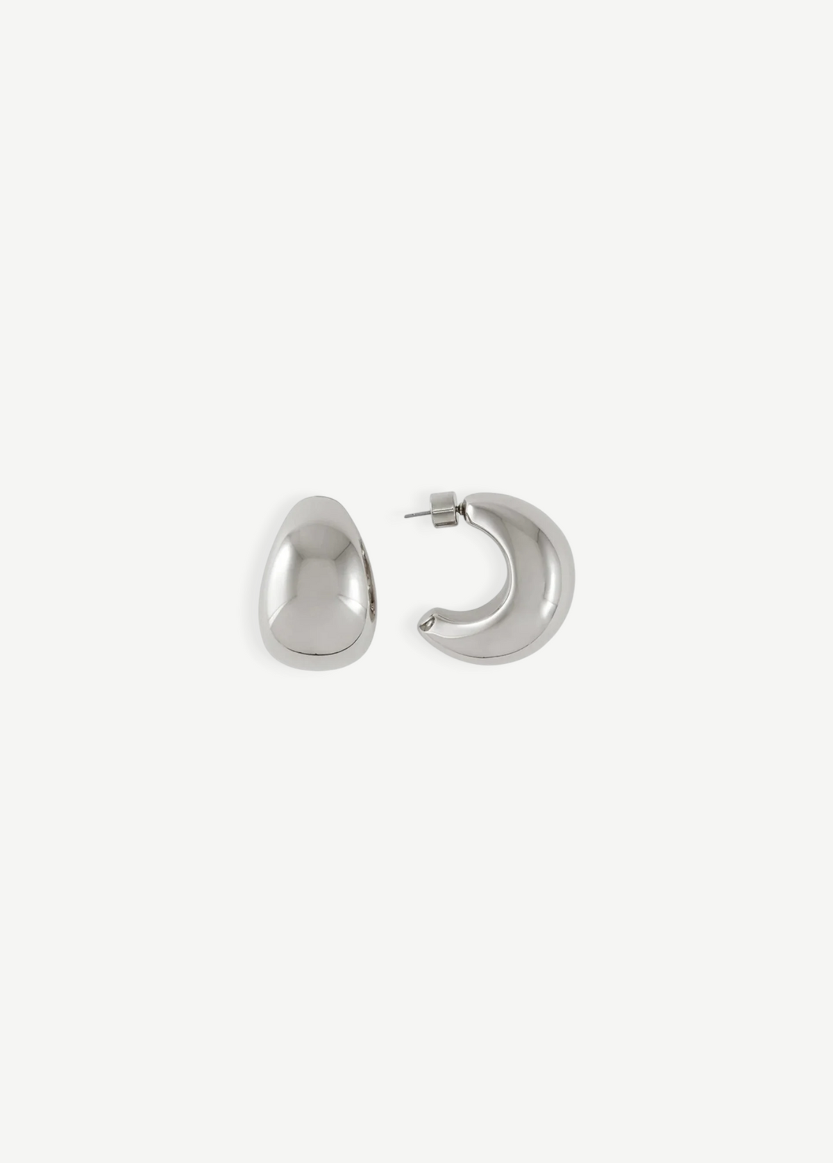 A pair of Jordyn Hoops in Rhodium—shiny, crescent-shaped stud earrings with pierced backs—are displayed against a plain white background, with one earring showing the front view and the other displaying the side profile.
