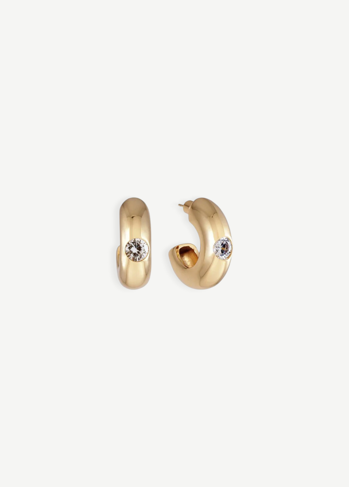 The Kaia Earrings are a pair of small, chunky gold plated hoops, each featuring a single round white gemstone accented with subtle crystal detailing, shown against a plain white background.