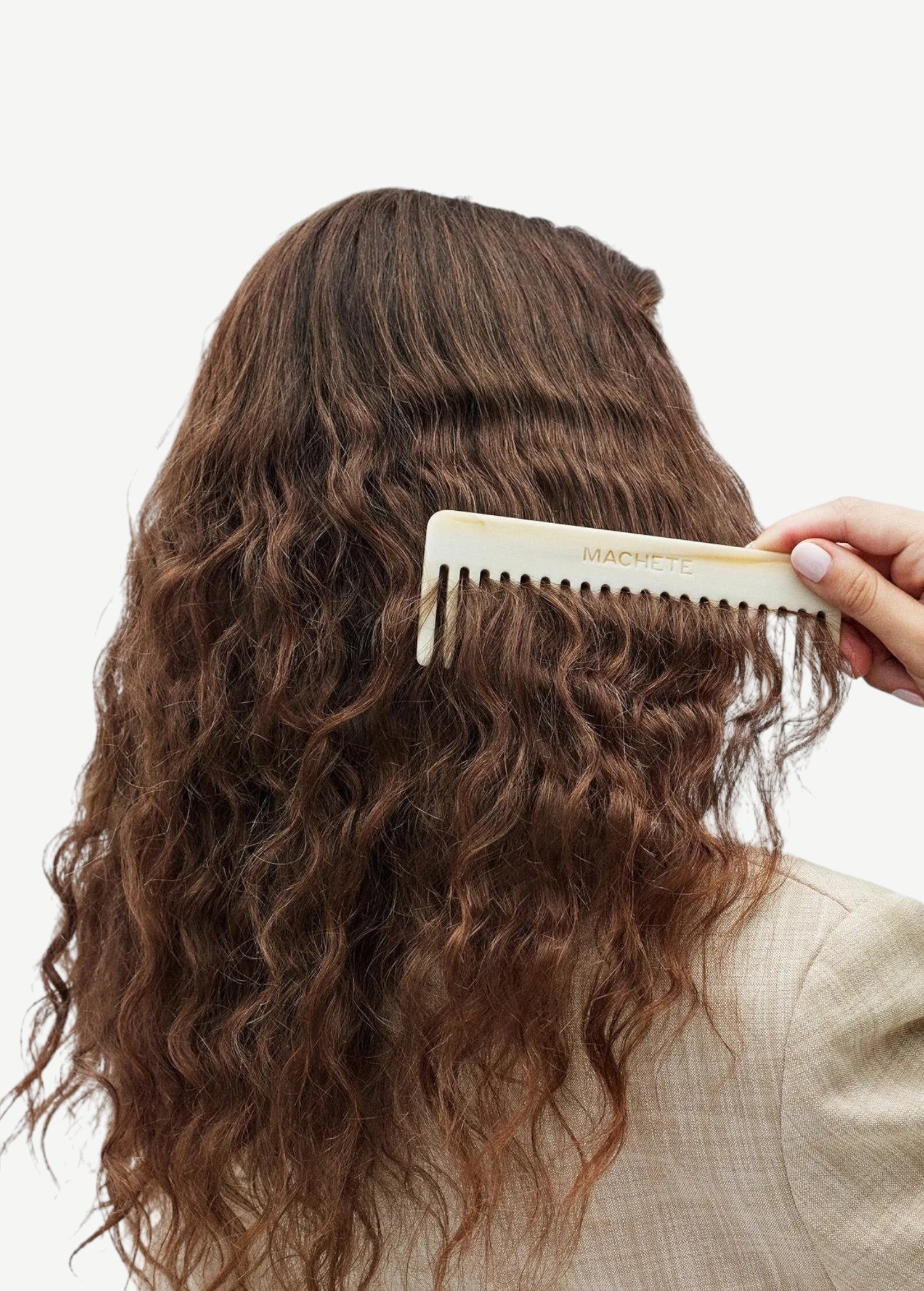 Person combing wavy hair with a white comb on a neutral background