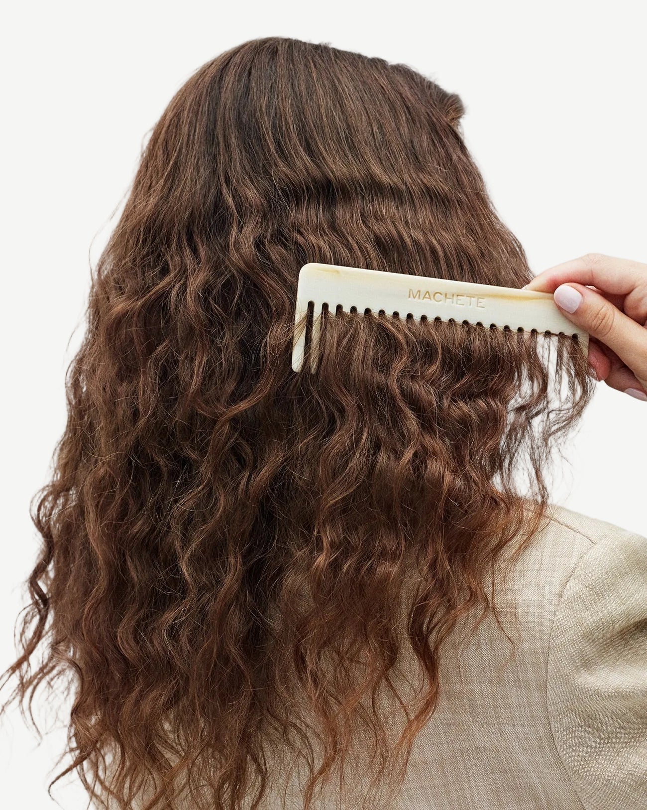 Person combing wavy hair with a white comb on a neutral background