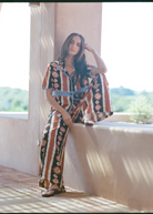 KABE SHOP INC Nera wide leg pants featuring a brown and white ikat print, worn by a woman in a sunny outdoor setting.