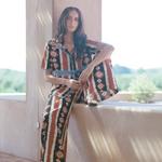 Woman wearing KABE SHOP INC Nera wide leg pants with a tribal ikat print in rust, cream, and black on a sunny patio.