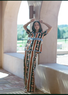 Woman wearing KABE SHOP INC Nera wide leg pants with a matching ikat print shirt in a sunlit arched corridor.
