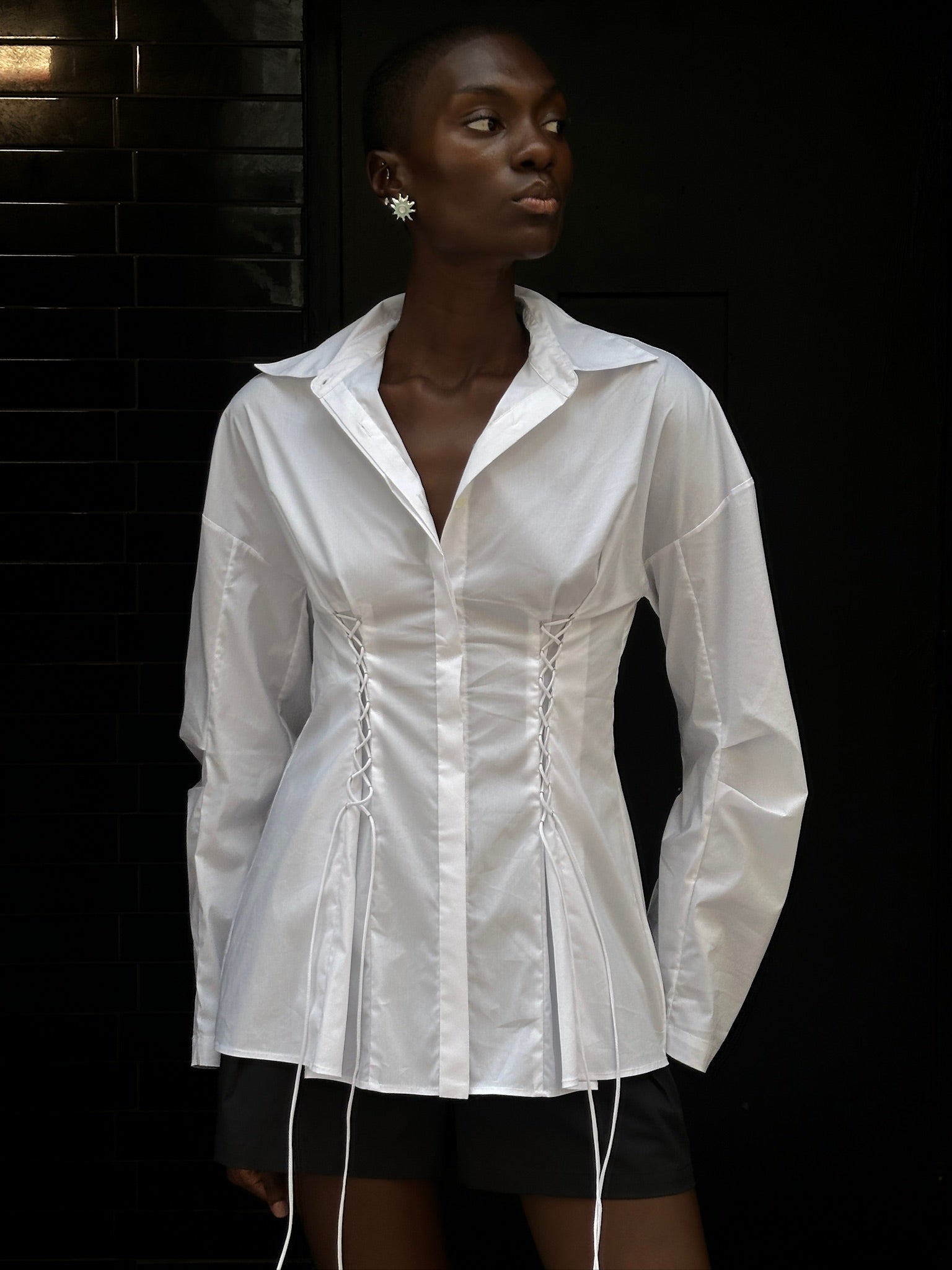 A person wears a white long-sleeve Laced Button Down featuring corset-style lace-up detailing at the waist to create a feminine silhouette.