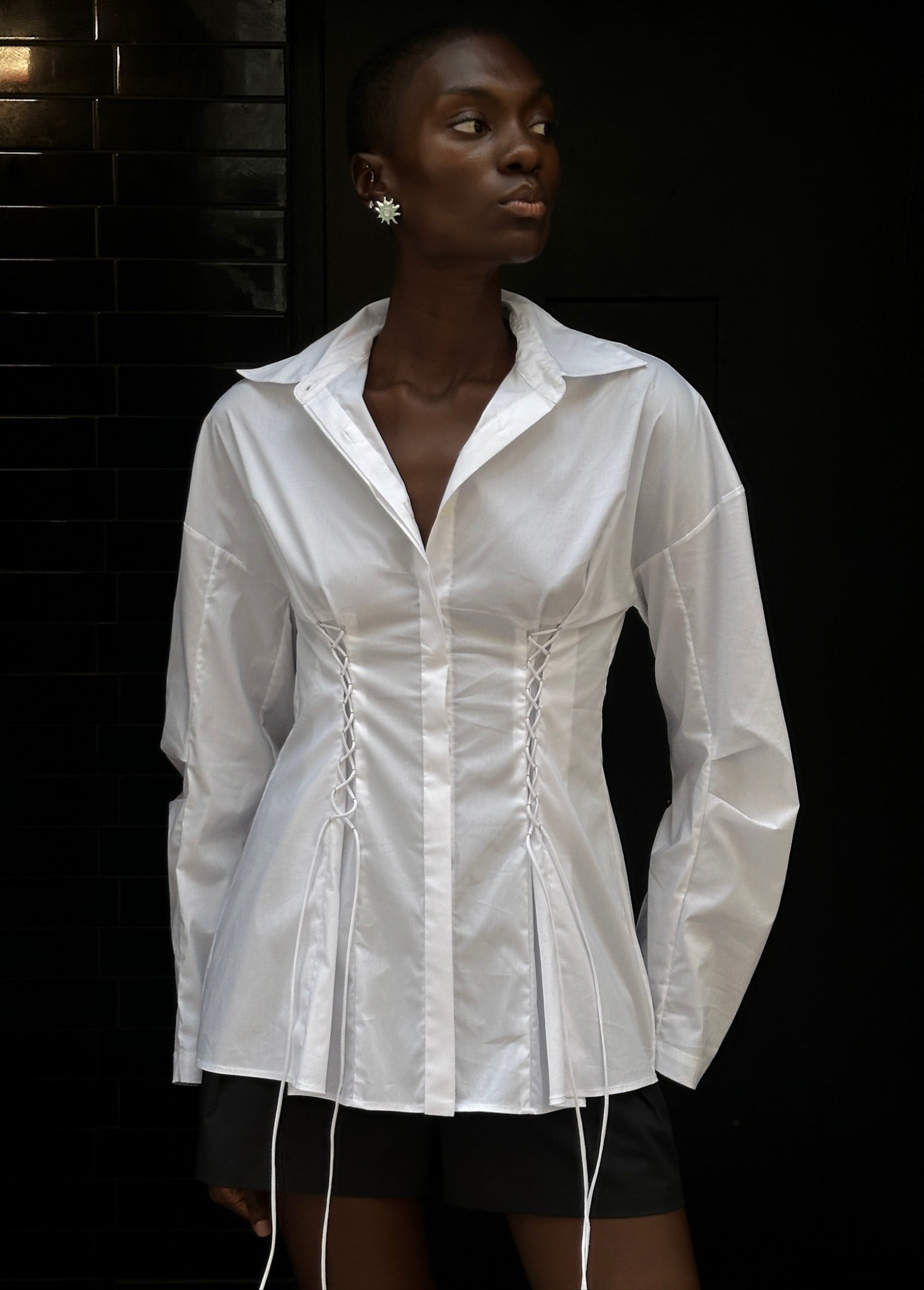 A person wears a white long-sleeve Laced Button Down featuring corset-style lace-up detailing at the waist to create a feminine silhouette.