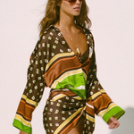 A person wearing a long-sleeved, geometric-patterned Cora Shirt, knotted at the waist over a bikini top.