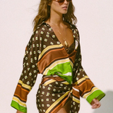 A person wearing a long-sleeved, geometric-patterned Cora Shirt, knotted at the waist over a bikini top.