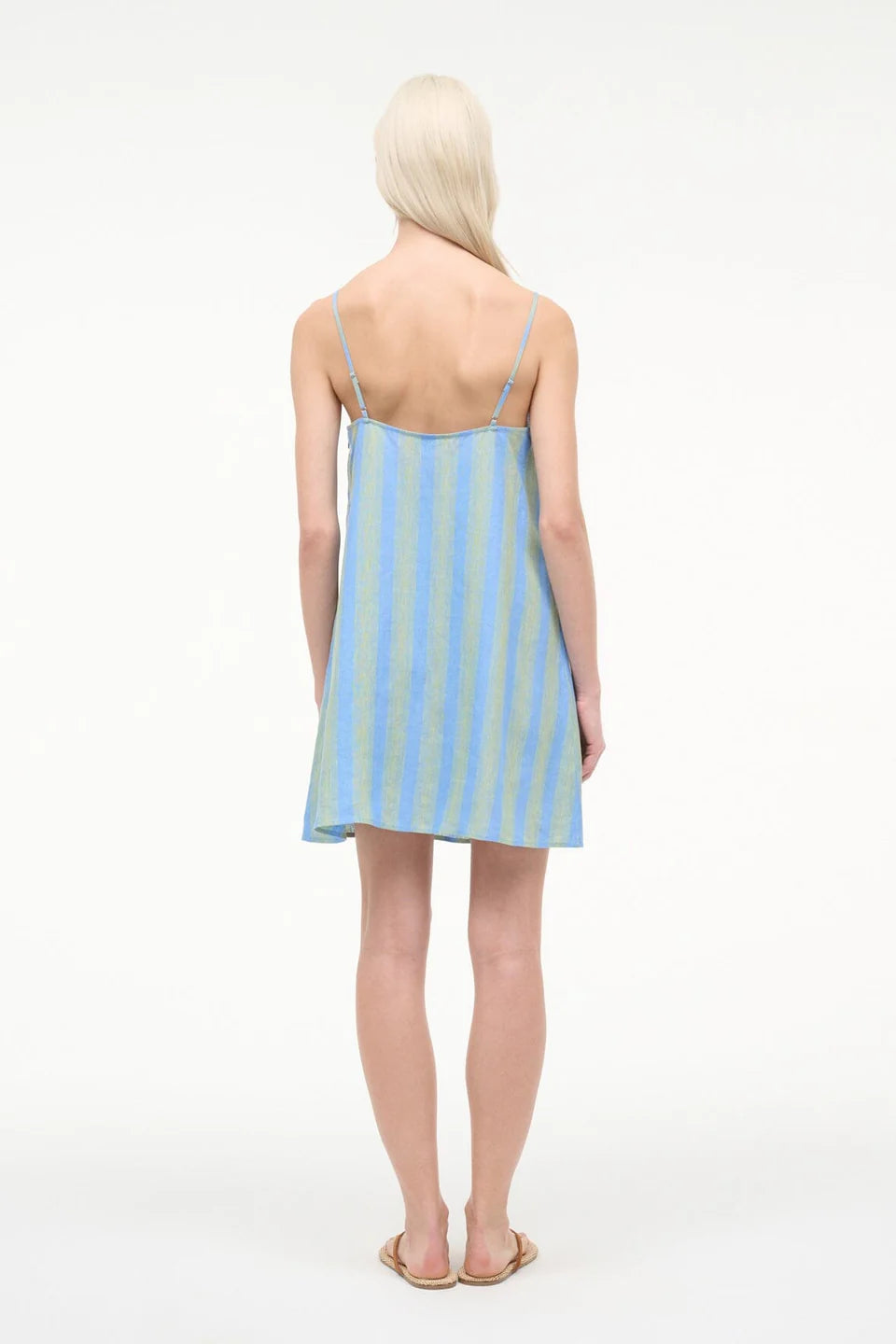 Back view of a person wearing a blue and green striped Laura Mini Dress with thin shoulder straps and flat sandals.