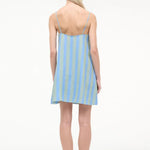 Back view of a person wearing a blue and green striped Laura Mini Dress with thin shoulder straps and flat sandals.