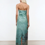Viewed from behind, a person wears the Amara Dress, a strapless, mint-green maxi featuring a photographic print of a coastal city at the hem and a back slit.