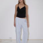 A person wears a black spaghetti strap camisole and light blue Deiji Studios Eyelet Pant, which are wide-leg pants with side eyelet detailing.