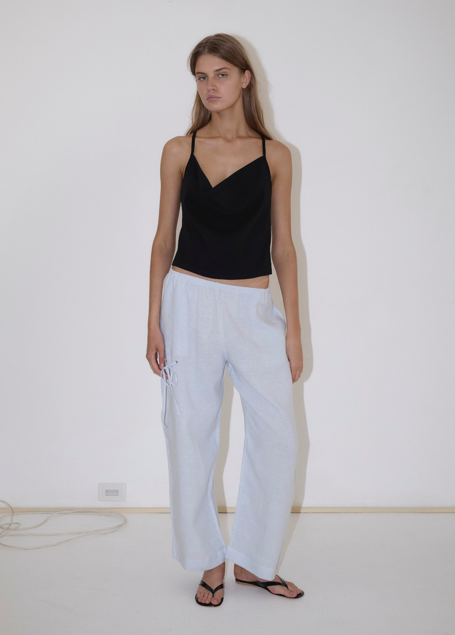 A person wears a black spaghetti strap camisole and light blue Deiji Studios Eyelet Pant, which are wide-leg pants with side eyelet detailing.