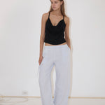 A person wearing a black camisole and light blue Deiji Studios Eyelet Pant, featuring a side drawstring and a straight-leg silhouette.