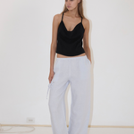 A person wearing a black camisole and light blue Deiji Studios Eyelet Pant, featuring a side drawstring and a straight-leg silhouette.