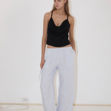 A person wearing a black camisole and light blue Deiji Studios Eyelet Pant, featuring a side drawstring and a straight-leg silhouette.
