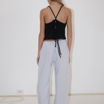 A person seen from behind wearing a black spaghetti-strap tank top with a tie back and light blue, straight-leg Eyelet Pant.