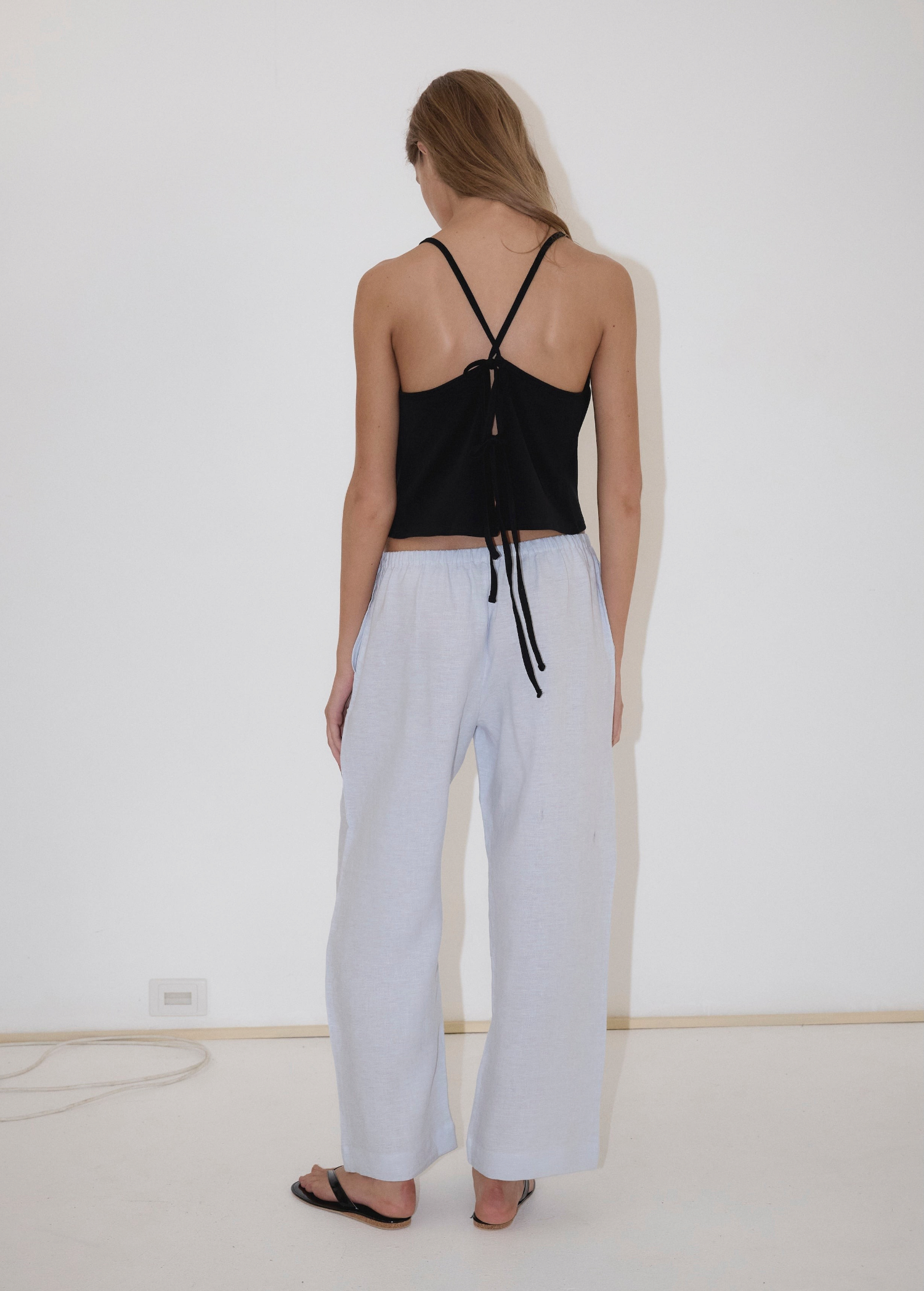 A person seen from behind wearing a black spaghetti-strap tank top with a tie back and light blue, straight-leg Eyelet Pant.