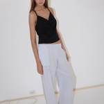 A person wearing a black camisole and white Eyelet Pant in a straight-leg silhouette, featuring loose-fitting fabric and a tied drawstring detail at the hip.