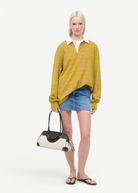 Model wearing a striped polo and denim skirt holding a KABE SHOP INC Maude shoulder bag with black and cream panels.