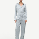 A person wears a matching light blue button-up shirt and Nami Pant wide-leg trousers in a crinkled, textured fabric that offers a relaxed silhouette.