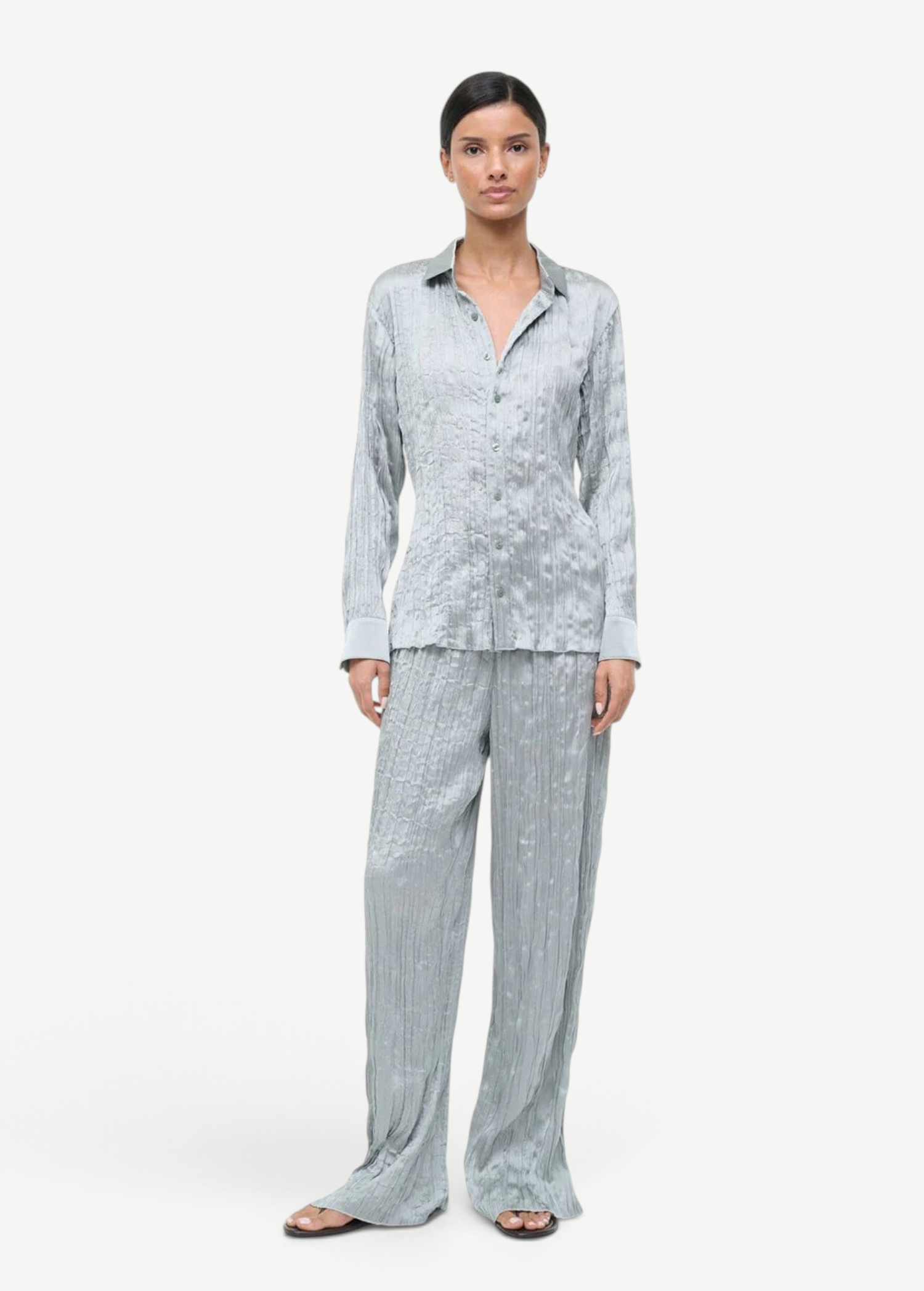 A person wears a matching light blue button-up shirt and Nami Pant wide-leg trousers in a crinkled, textured fabric that offers a relaxed silhouette.