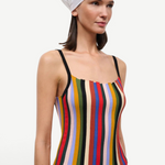 A person wearing a versatile Skye Tank with a square neckline, vertical multicolored stripes, and thin black straps, paired with a white headscarf and jeans.