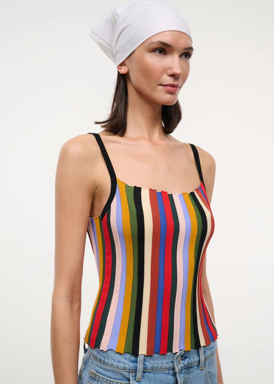 A person wearing a versatile Skye Tank with a square neckline, vertical multicolored stripes, and thin black straps, paired with a white headscarf and jeans.