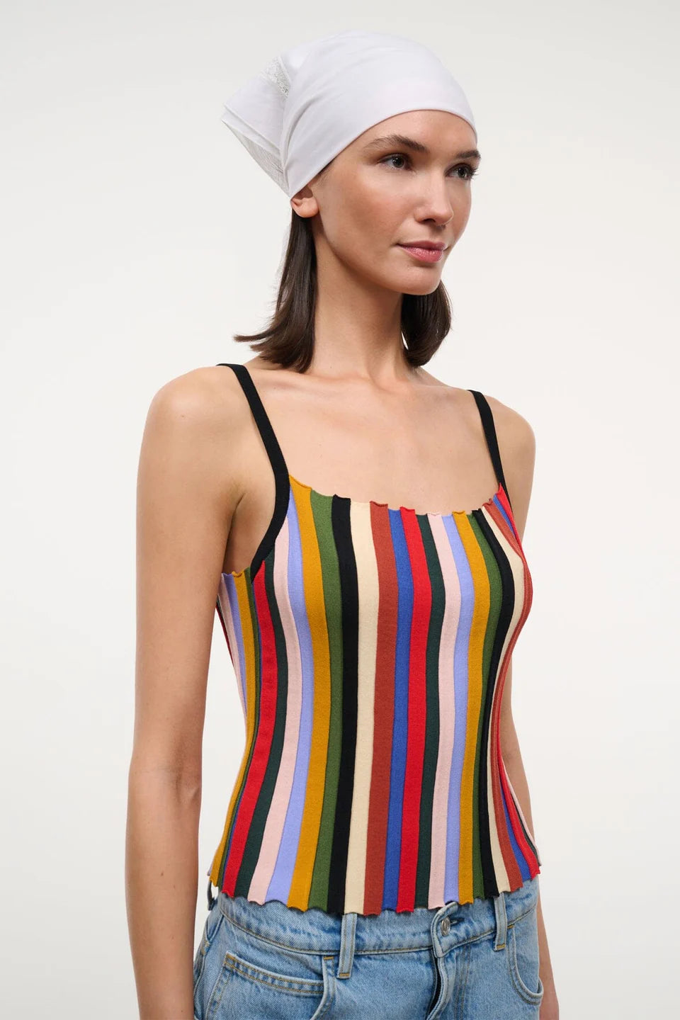 A person wearing a versatile Skye Tank with a square neckline, vertical multicolored stripes, and thin black straps, paired with a white headscarf and jeans.