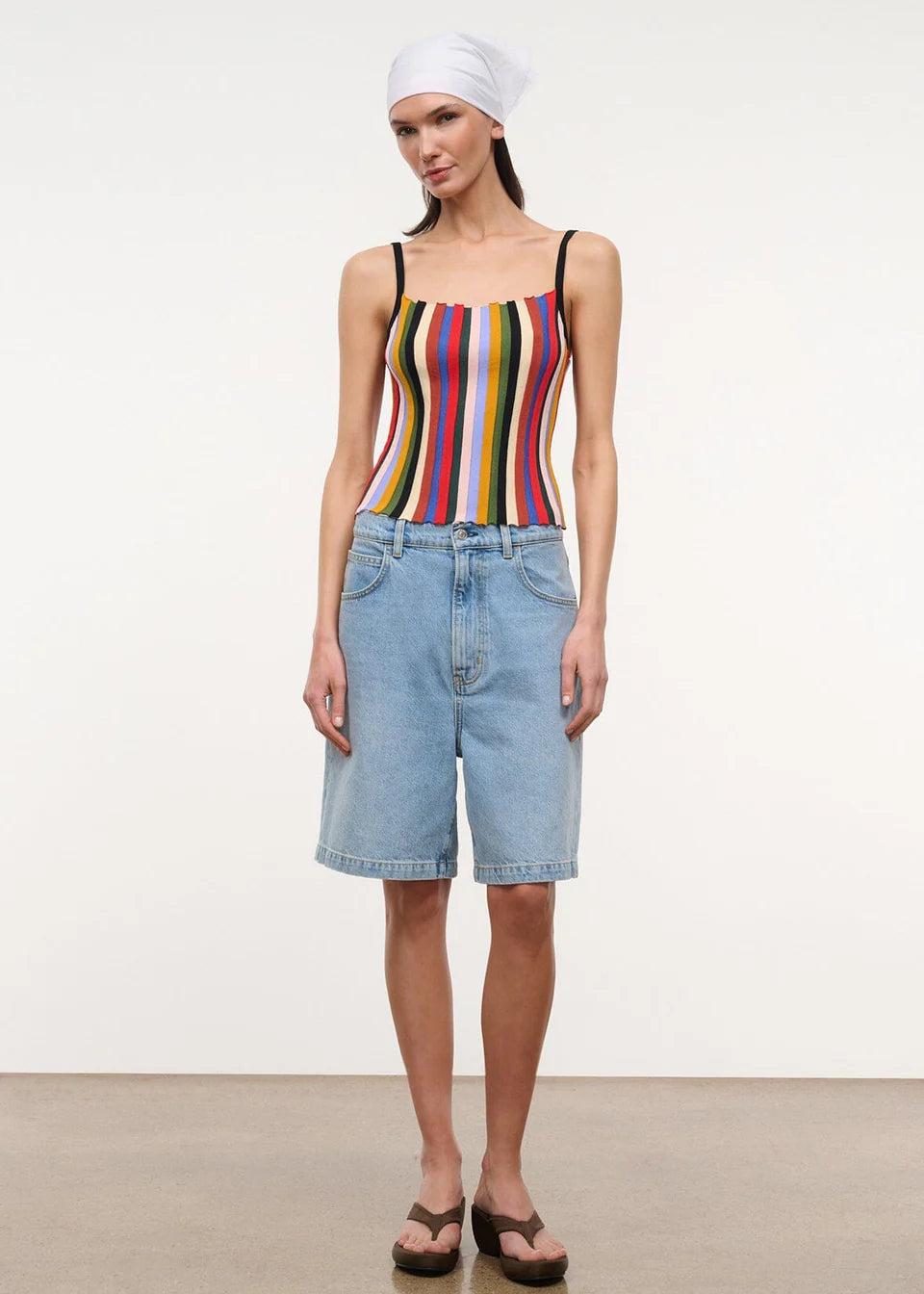 A person wears a multicolored, vertically striped Skye Tank, light-wash denim shorts, and brown platform flip-flops.