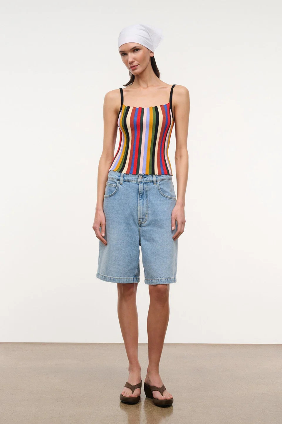 A person wears a multicolored, vertically striped Skye Tank, light-wash denim shorts, and brown platform flip-flops.