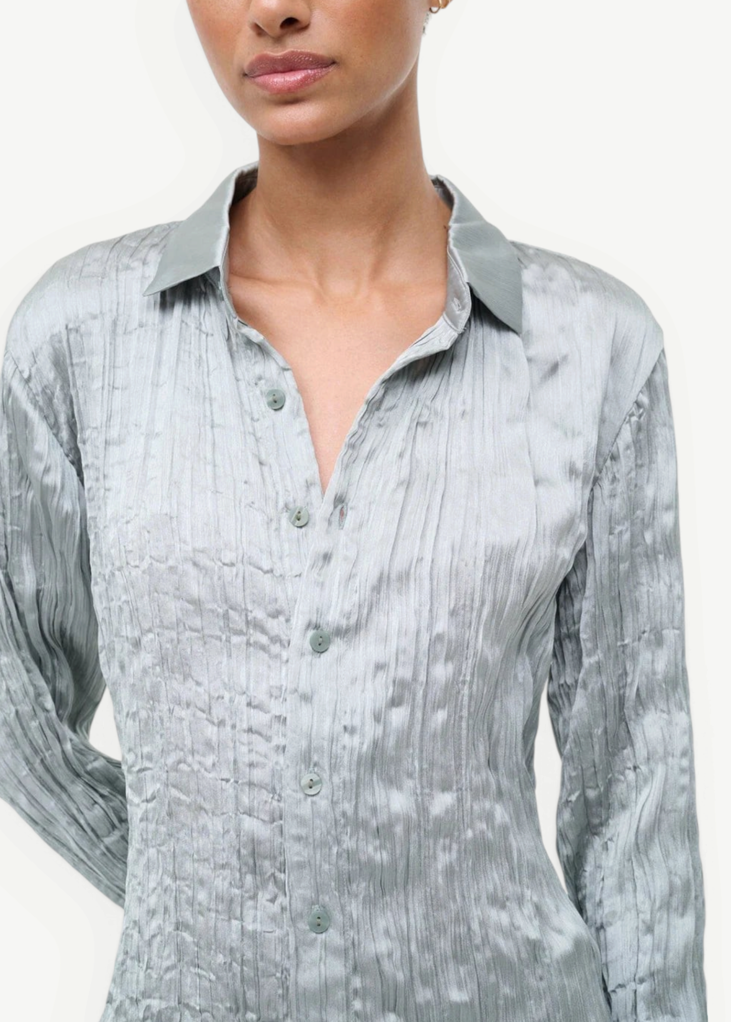 A person wearing the Suki Shirt, a sage green button-up with a long-sleeved, crinkled texture that serves as a versatile wardrobe essential.