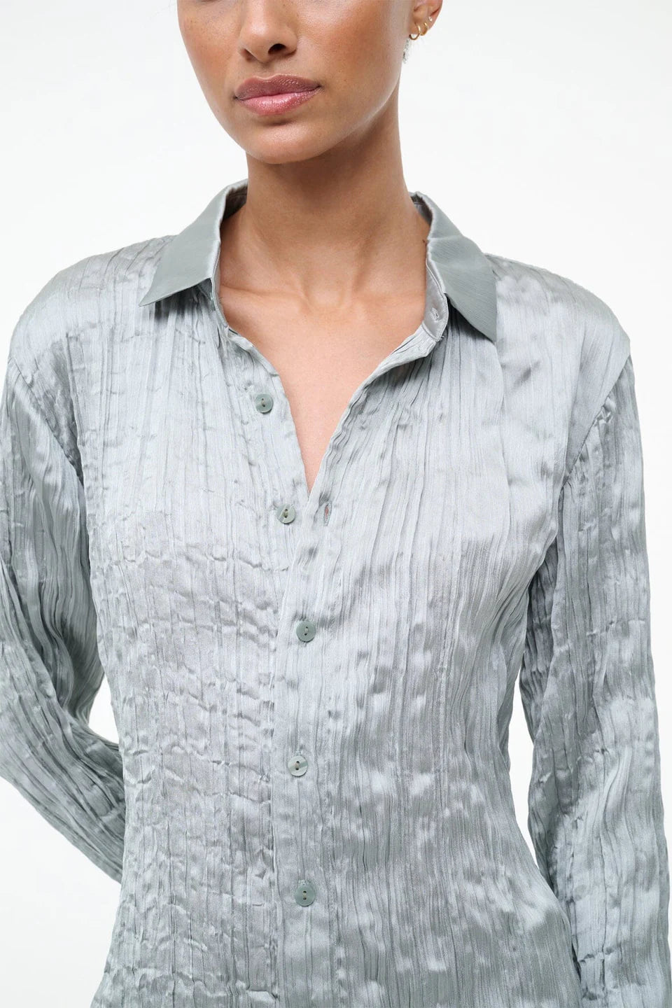 A person wearing the Suki Shirt, a sage green button-up with a long-sleeved, crinkled texture that serves as a versatile wardrobe essential.