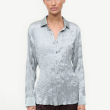 A model wearing the Suki Shirt, a light sage, long-sleeved button-down with a crinkled texture that serves as a versatile wardrobe essential.