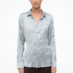 A model wearing the Suki Shirt, a light sage, long-sleeved button-down with a crinkled texture that serves as a versatile wardrobe essential.
