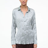 A model wearing the Suki Shirt, a light sage, long-sleeved button-down with a crinkled texture that serves as a versatile wardrobe essential.