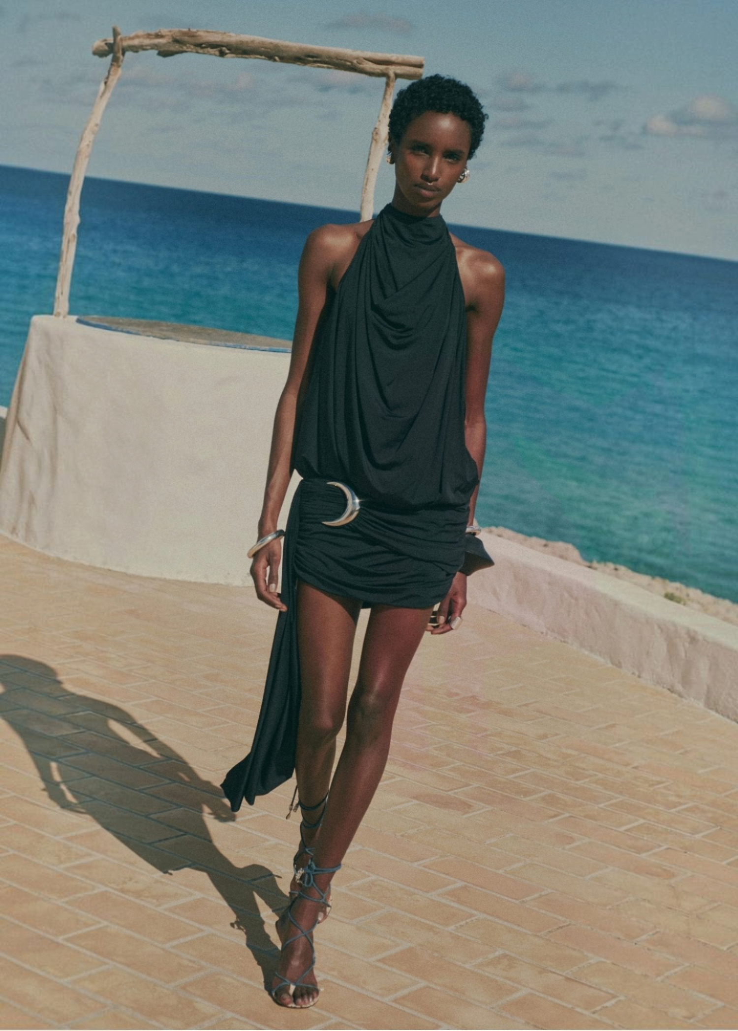 KABE SHOP INC Vida mini dress in black stretch jersey with a halterneck, cowl back, and silver crescent moon hardware.