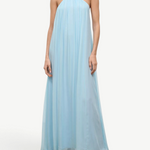 A floor-length, light blue Dasha Dress with a pleated halter-neck design, styled with silver strappy sandals for a minimalist summer look.